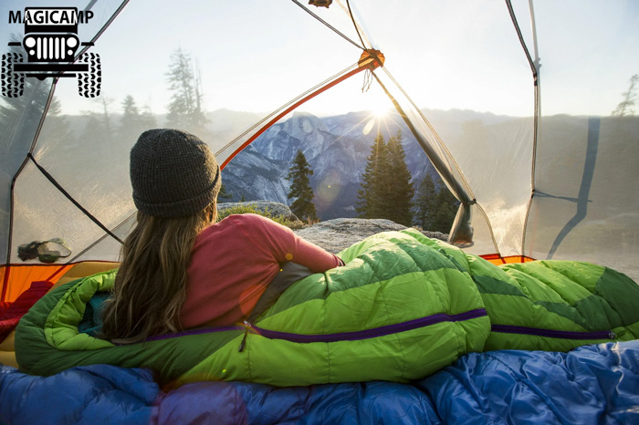 دختری در کیسه خواب در یک چادر در حال تماشای طلوع آفتاب
